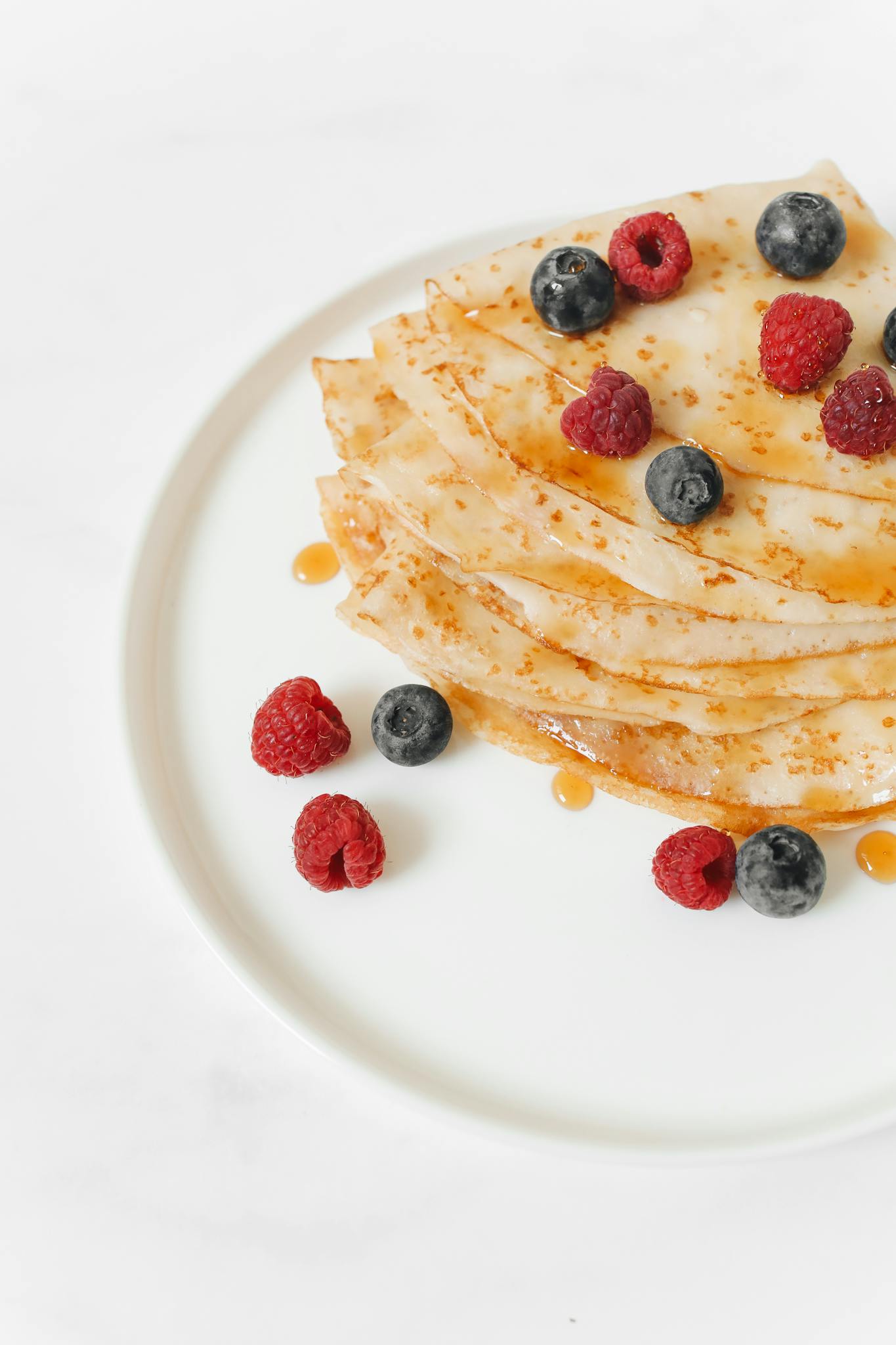 A stack of homemade pancakes topped with fresh berries and syrup on a white plate.