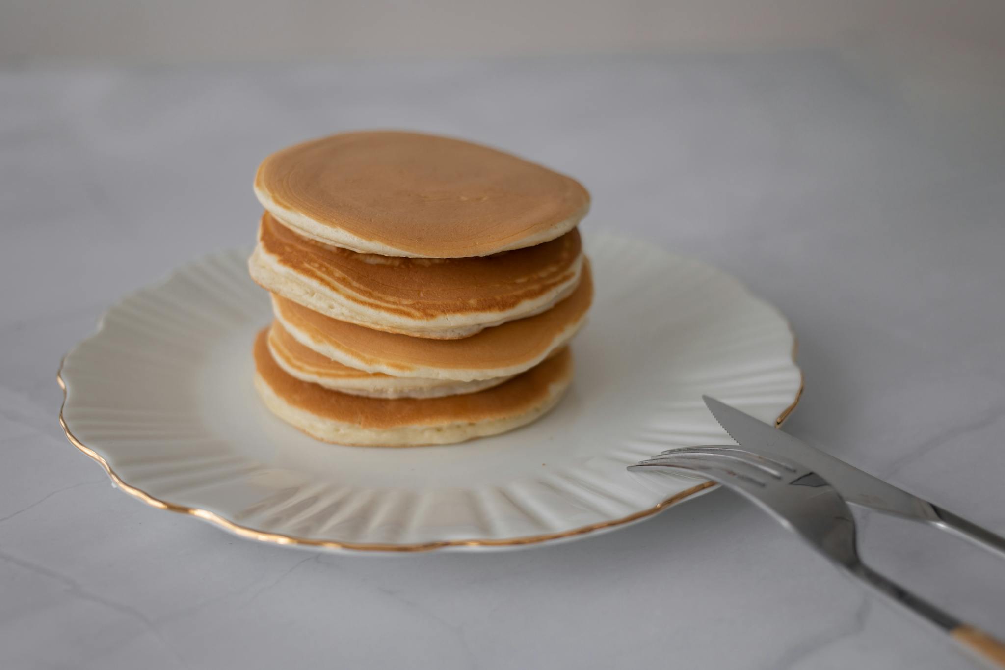 A stack of pancakes elegantly presented on a white plate with cutlery, perfect for breakfast themes.