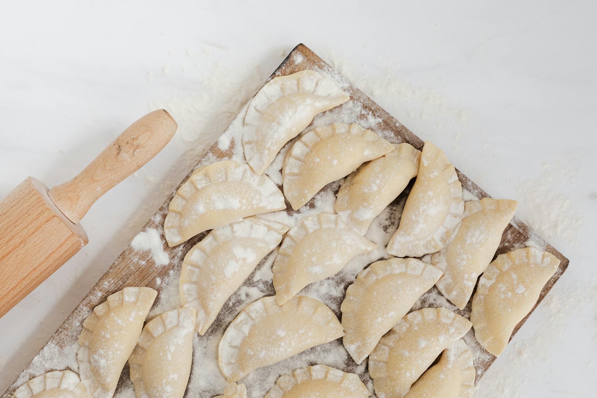 Close-up of homemade pierogi dumplings on a wooden board, dusted with flour, ready for cooking.